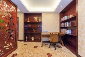 Una habitación con escritorio, estanterías llenas de libros, objetos decorativos y una alfombra estampada.