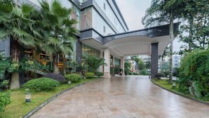 Un edificio espacioso y moderno con una entrada curva, rodeado de abundante vegetación y palmeras.
