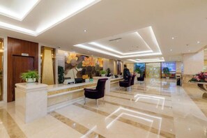 Een moderne hotellobby met een receptiebalie, een zithoek en een grote bloemenmuur.