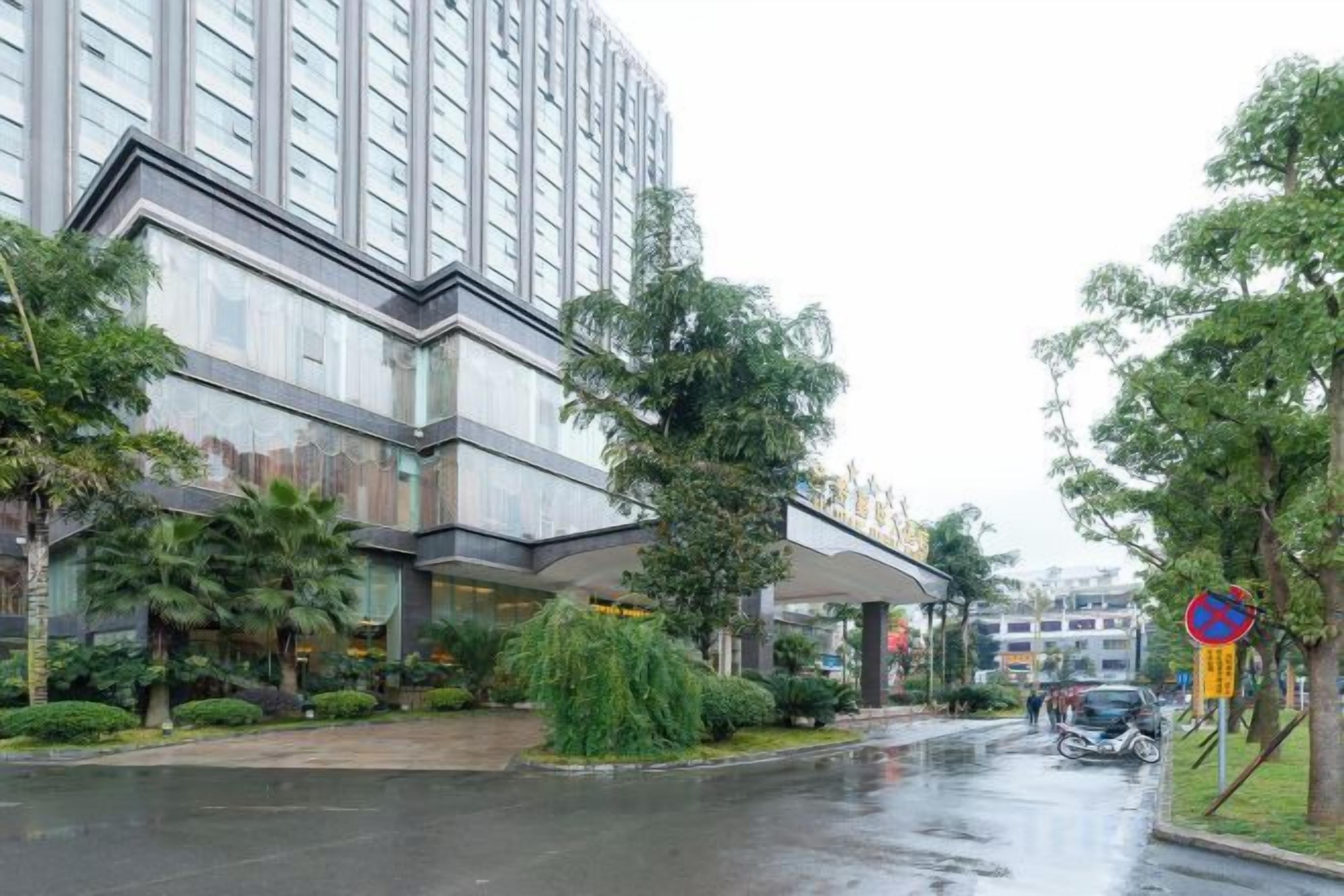 A modern hotel with a glass facade, a covered entrance, and a parking area with cars.