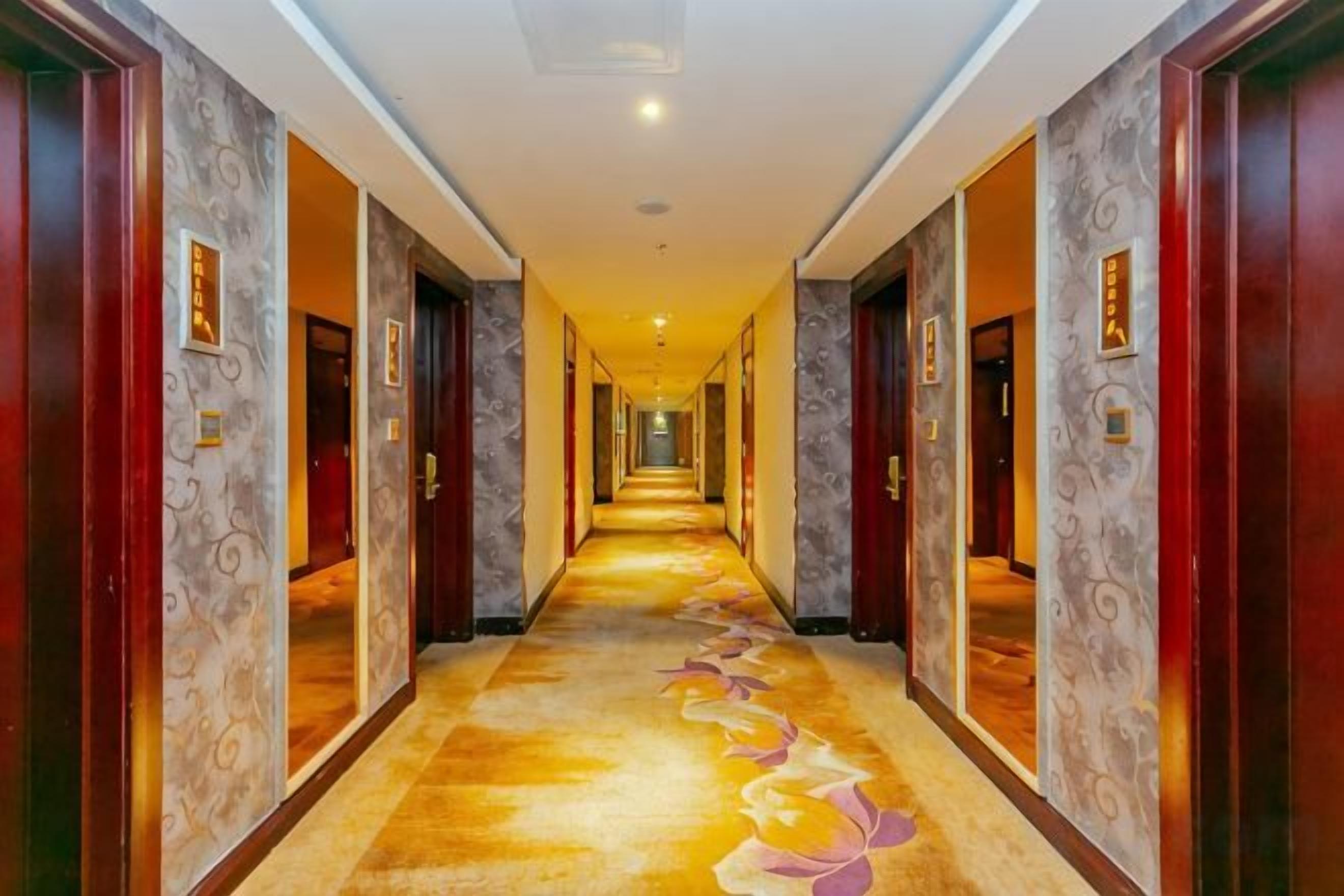 Un pasillo de hotel con puertas a ambos lados, una alfombra estampada y una lámpara en el techo.