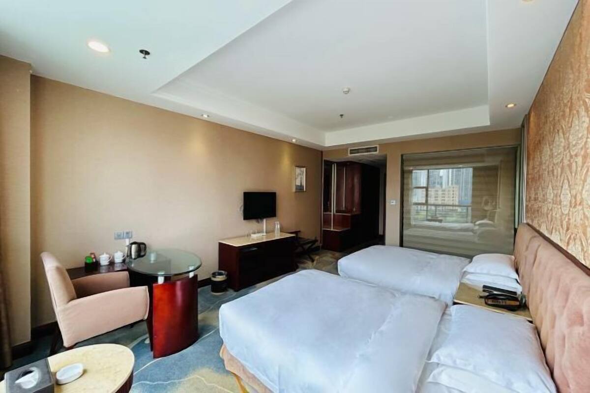 Een hotelkamer met twee bedden, een bureau, een stoel, een televisie en een groot raam.