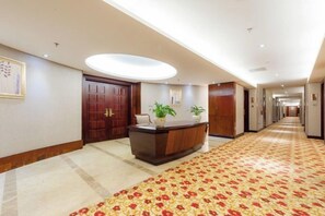 Un hall d’hôtel avec un comptoir d’accueil, une grande porte en bois et un tapis à motifs.