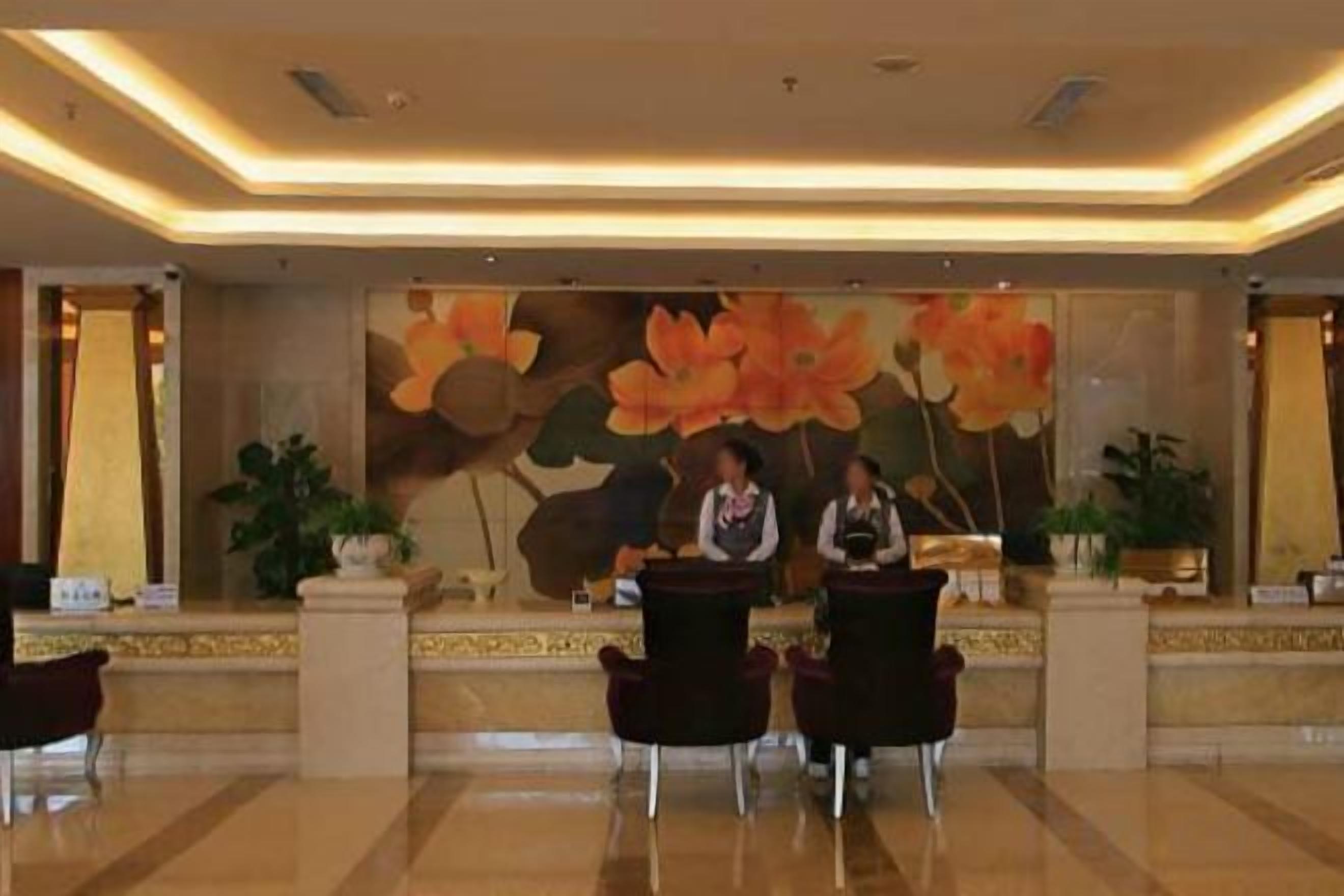 A hotel reception area with a large floral mural, a reception desk, and several chairs.