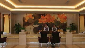 A hotel reception area with a large floral mural, a reception desk, and several chairs.