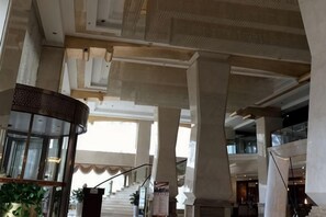 Un interior espacioso con techos altos, grandes columnas y una escalera que conduce a un nivel superior.