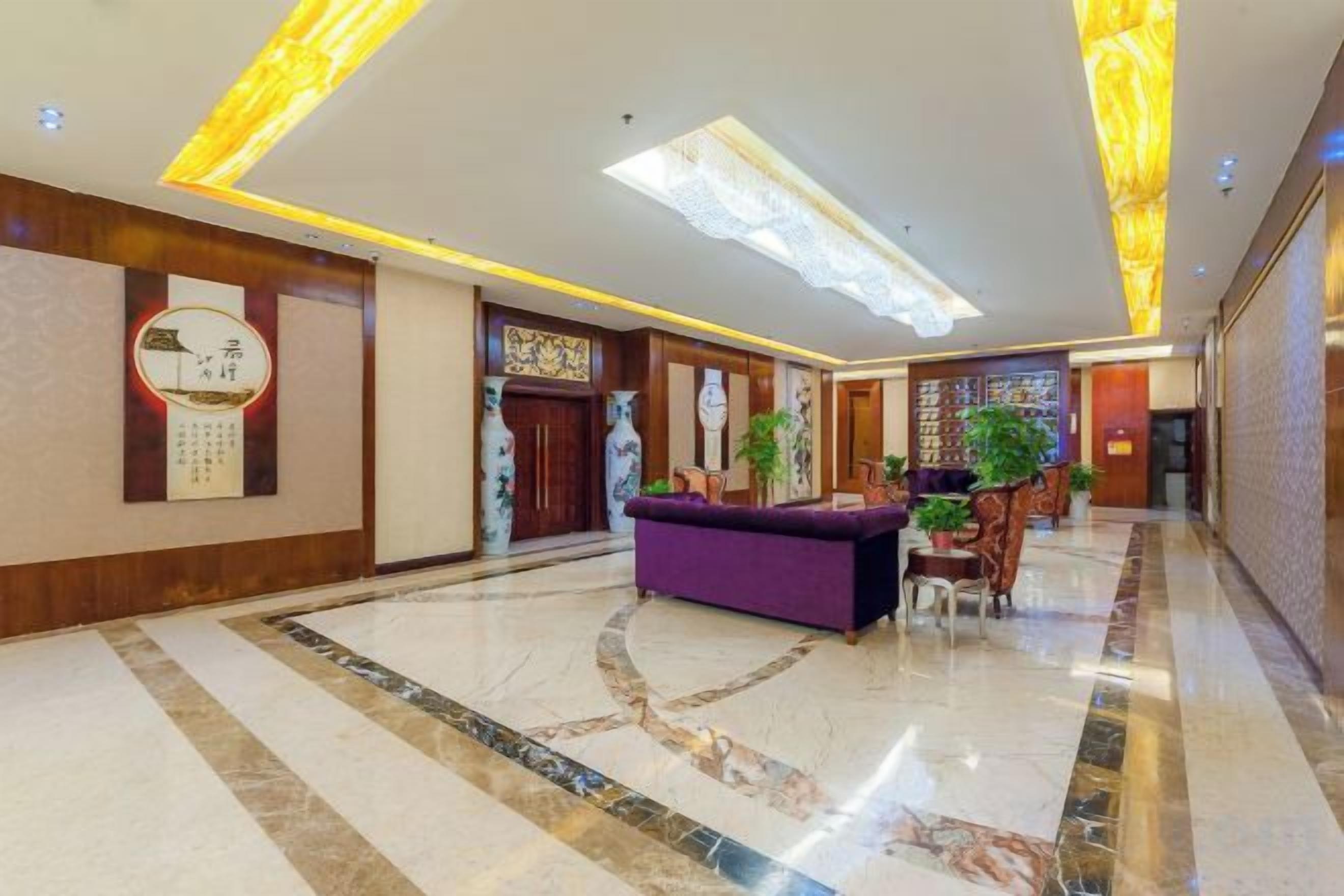 A hotel lobby with a reception desk, a large chandelier, and a marble floor.