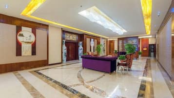 A hotel lobby with a reception desk, a large chandelier, and a marble floor.