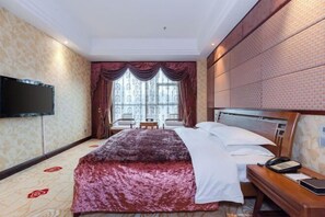 Habitació d'hotel amb un llit gran, televisió penjada a la paret, escriptori amb un telèfon i finestra amb cortines.