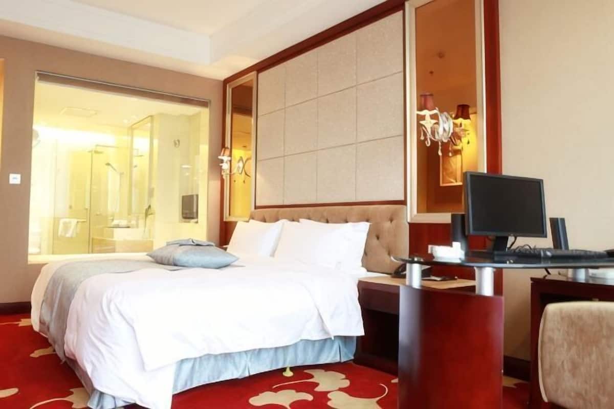 Hotelkamer met een bed, een bureau met een computer, een stoel en een badkamer zichtbaar door een glazen deur.