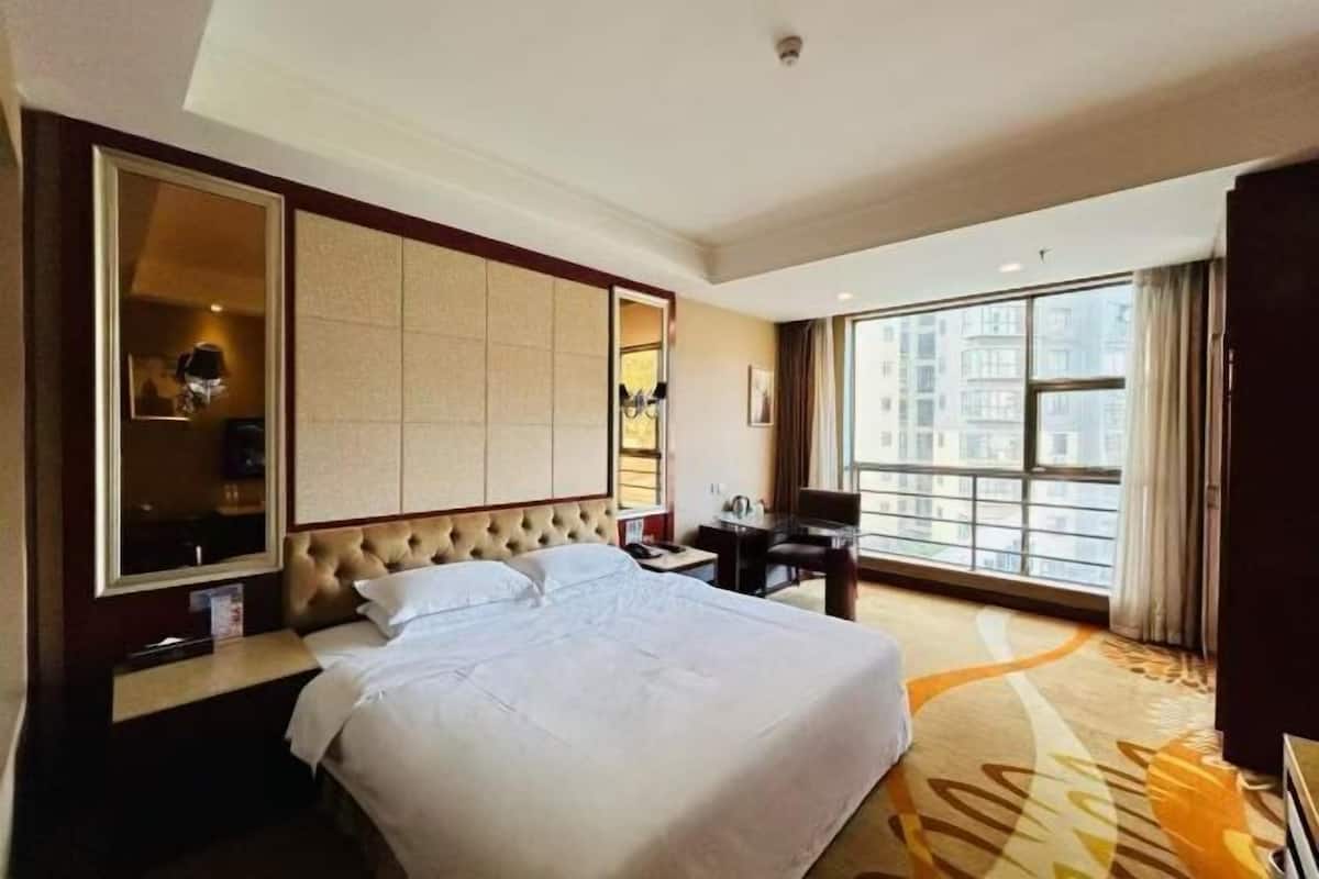 Hotelkamer met een groot bed, een bureau, een stoel, een grote spiegel en uitzicht op de stad.