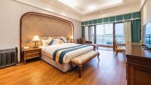 A hotel room with a large bed, a desk, a chair, a bench, a nightstand, and a window with curtains. - Tianju Caohai Holiday Hotel (Weining)