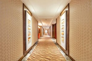 Un couloir d’hôtel avec un tapis à motifs, des tableaux encadrés accrochés aux murs et des portes donnant accès aux chambres.