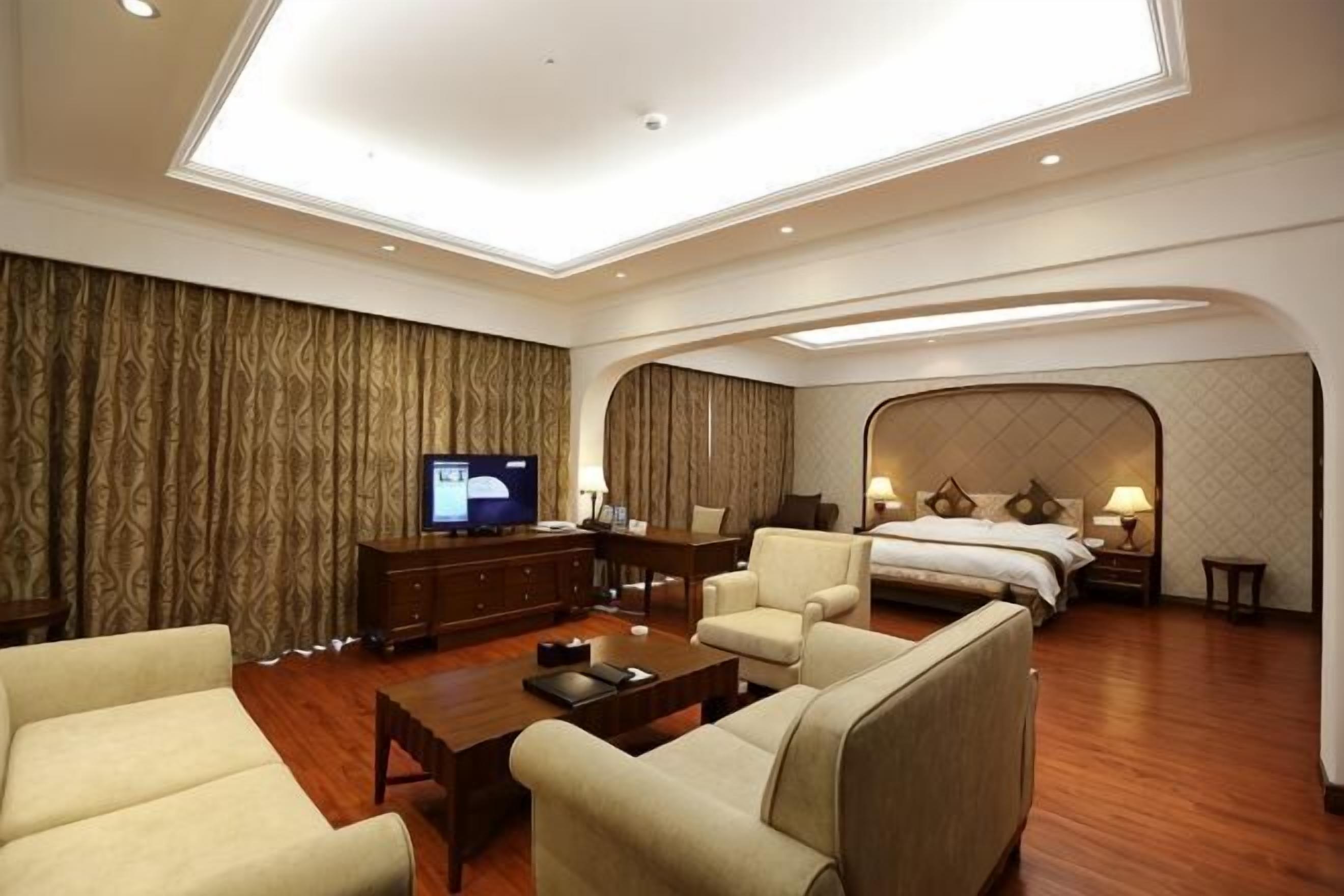 Ein Hotelzimmer mit einem großen Bett, einem Fernseher, einer Couch, einem Couchtisch und einer Deckenleuchte.