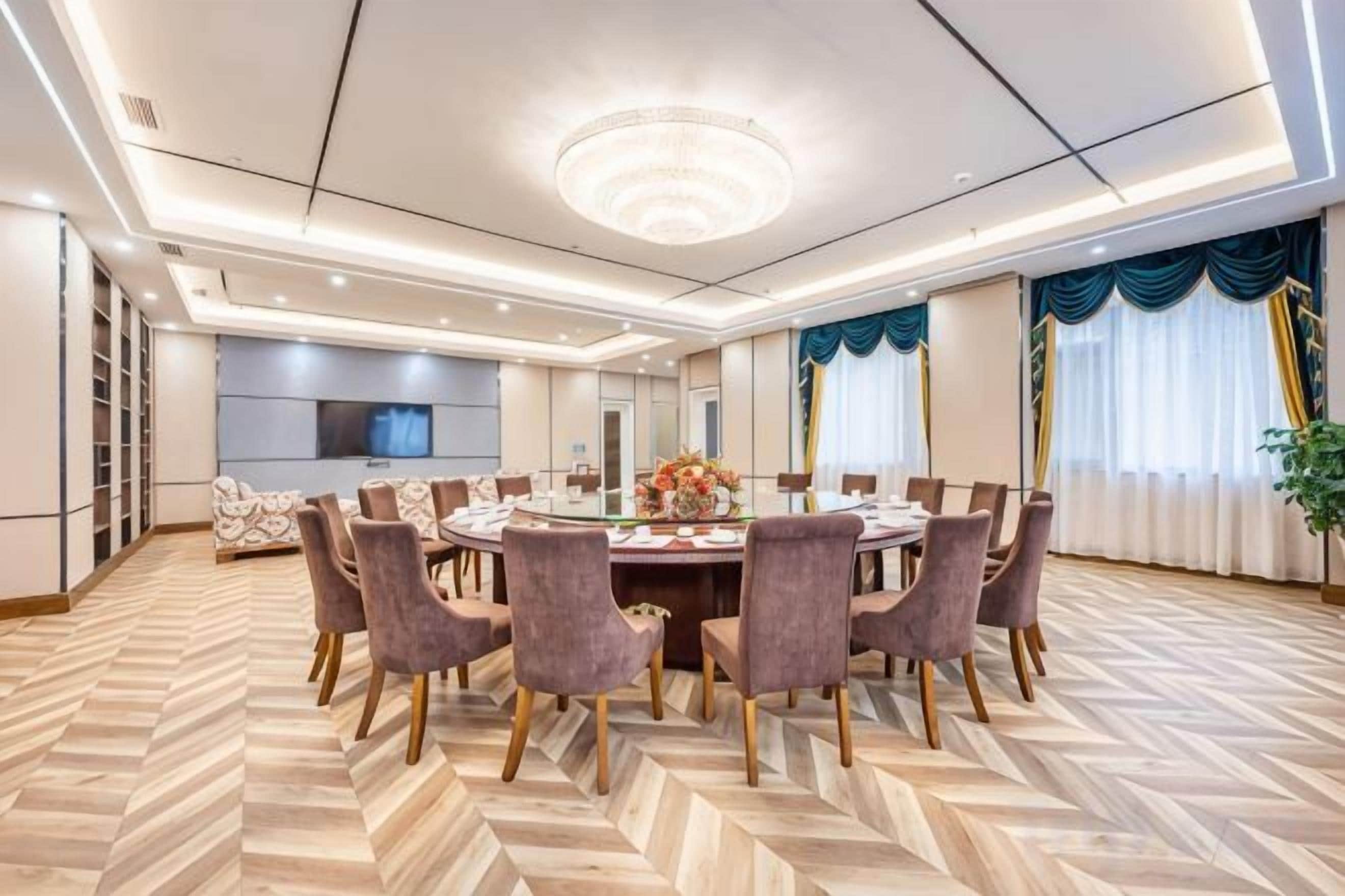 Sala de conferência com mesa redonda, cadeiras e tela de televisão.