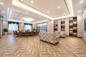A spacious room with a herringbone floor pattern, a dining area with a round table and chairs, a patterned sofa, and built-in shelving with books.