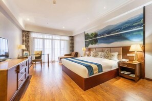 Une chambre d’hôtel avec un grand lit, un bureau, une chaise, une télévision et un tableau au mur.