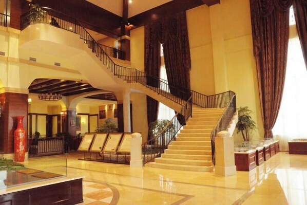 A spacious lobby with a grand staircase, a reception desk, and seating areas. - Tianju Caohai Holiday Hotel (Weining)
