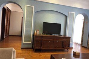 A living room with a flat-screen TV on a wooden cabinet, a sofa, and a coffee table. - Tianju Caohai Holiday Hotel (Weining)