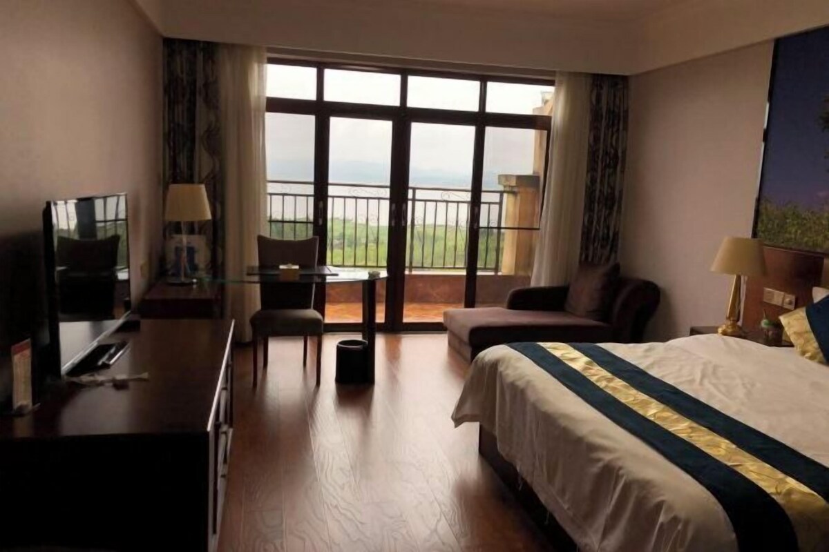 A hotel room with a bed, a desk, a chair, and a balcony with a view.