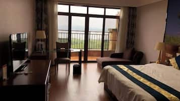 A hotel room with a bed, a desk, a chair, and a balcony with a view.