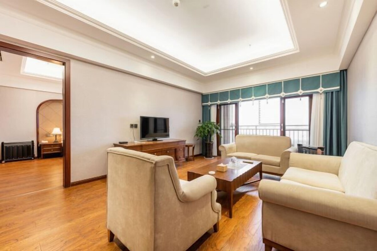 A spacious living room with a flat-screen TV, two sofas, a coffee table, and a large window with curtains.