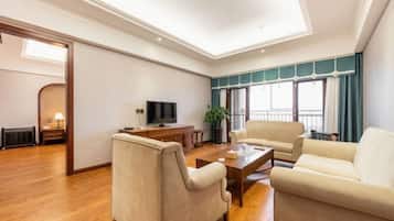 A spacious living room with a flat-screen TV, two sofas, a coffee table, and a large window with curtains.