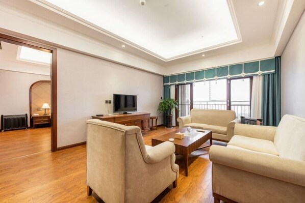 A spacious living room with a flat-screen TV, two sofas, a coffee table, and a large window with curtains. - Tianju Caohai Holiday Hotel (Weining)