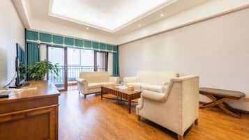 A spacious living room with a wooden coffee table, two white sofas, a wooden desk, and a large window with teal curtains.