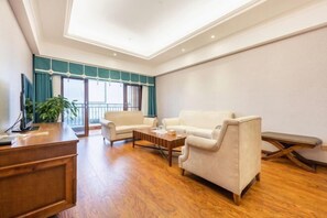 A spacious living room with a wooden coffee table, two white sofas, a wooden desk, and a large window with teal curtains. - Tianju Caohai Holiday Hotel (Weining)