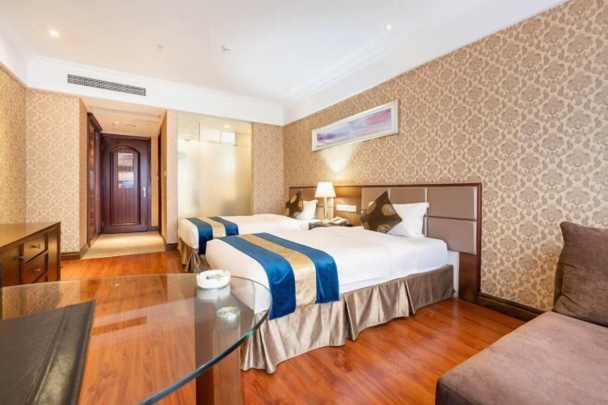 A hotel room with two beds, a desk, and a glass table.