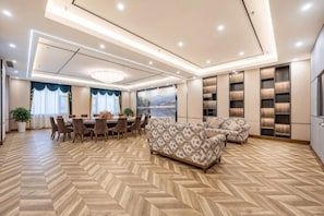 Ein geräumiges Zimmer mit Fischgrätparkett, einem Essbereich mit rundem Tisch und Stühlen, einem gemusterten Sofa und eingebauten Regalen mit Büchern.