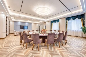 Une salle de conférence équipée d’une table ronde, de chaises, d’un lustre et d’un écran de télévision.