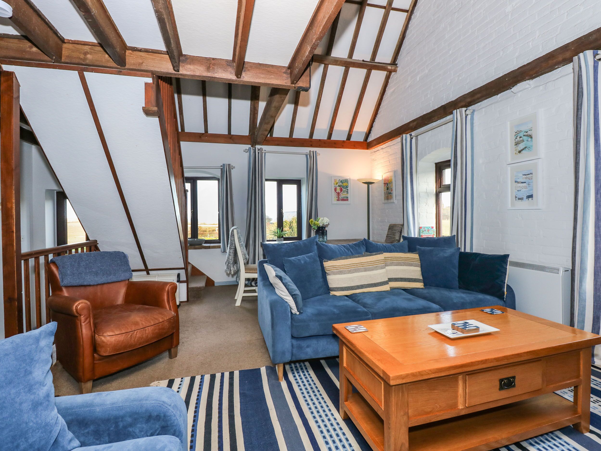Une pièce confortable de style loft, avec un plafond en bois, un canapé bleu, un fauteuil en cuir marron et une table basse en bois.