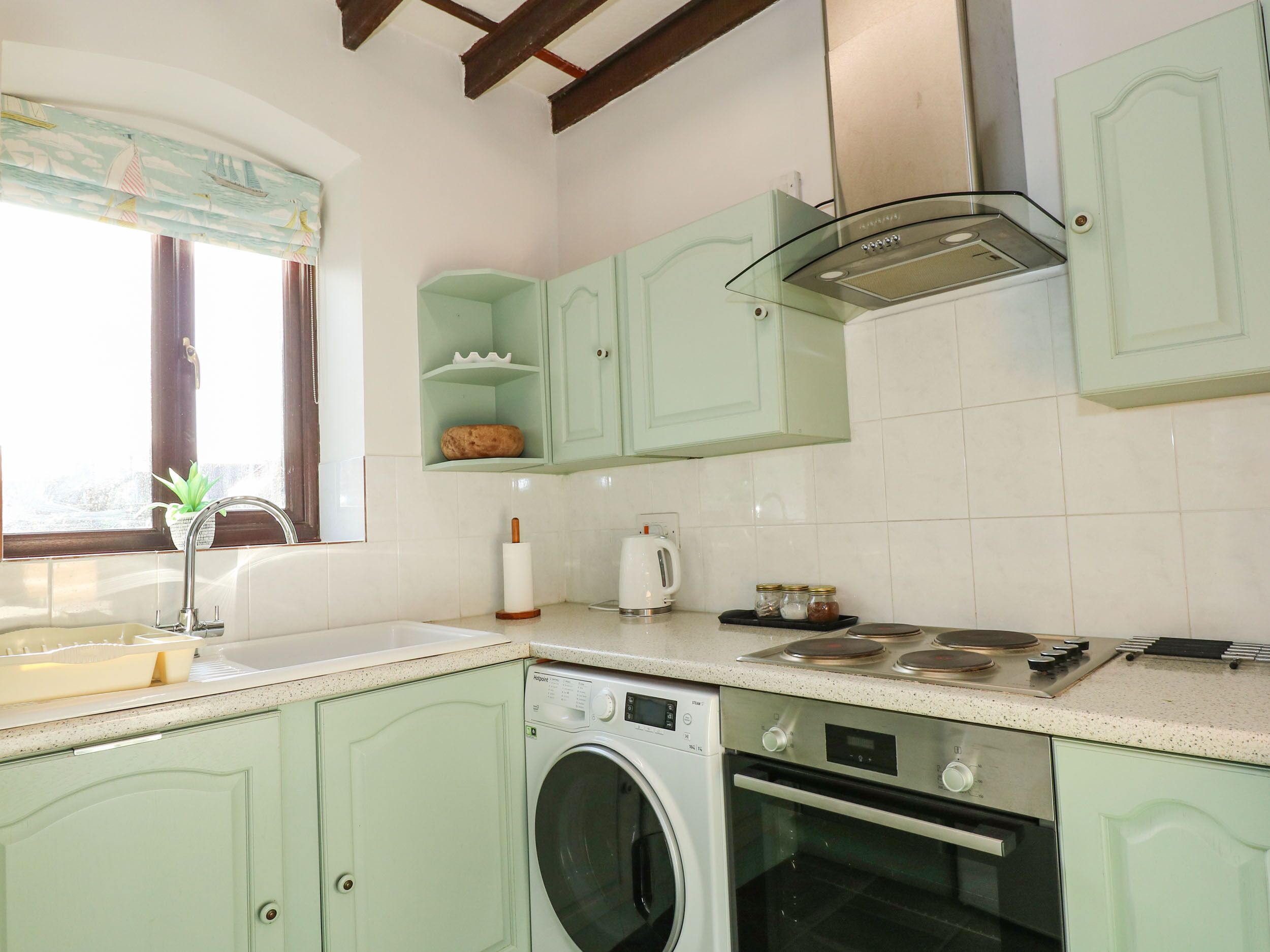 A kitchen with light green cabinets, a washing machine, an oven, and a window with curtains.