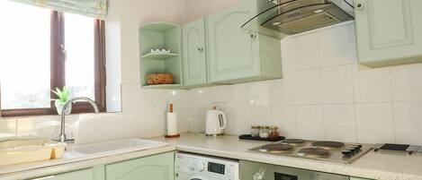 A kitchen with light green cabinets, a washing machine, an oven, and a window with curtains.