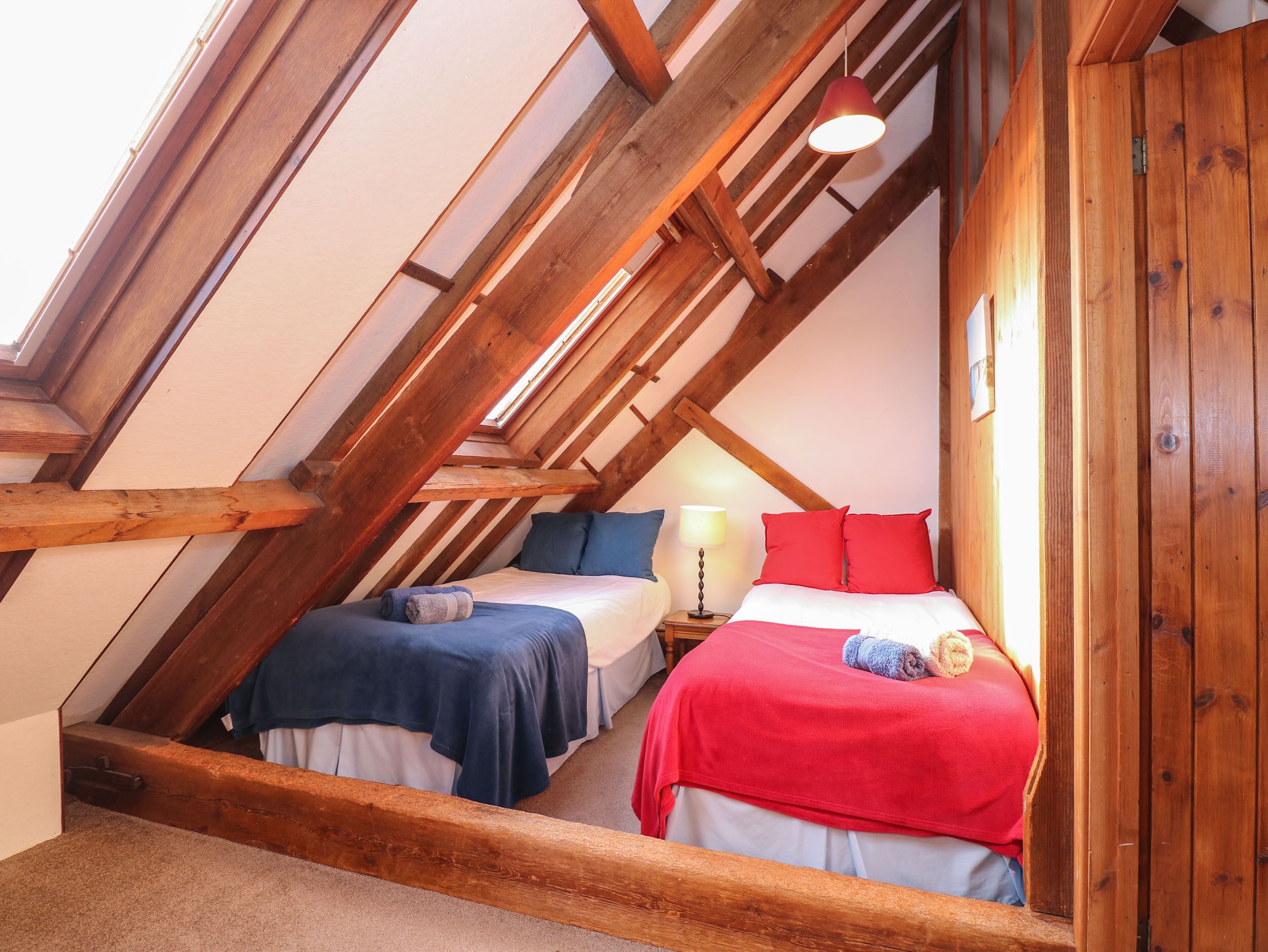 A dormitory room with two beds, wooden beams, a skylight, and a red lamp.