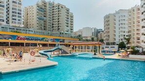 A swimming pool area with a lifeguard stand, lounge chairs, and a building with a 'Zoomarine' sign. - Kojima Lilac Apartament, Praia da Rocha, Portimao (Portimão)