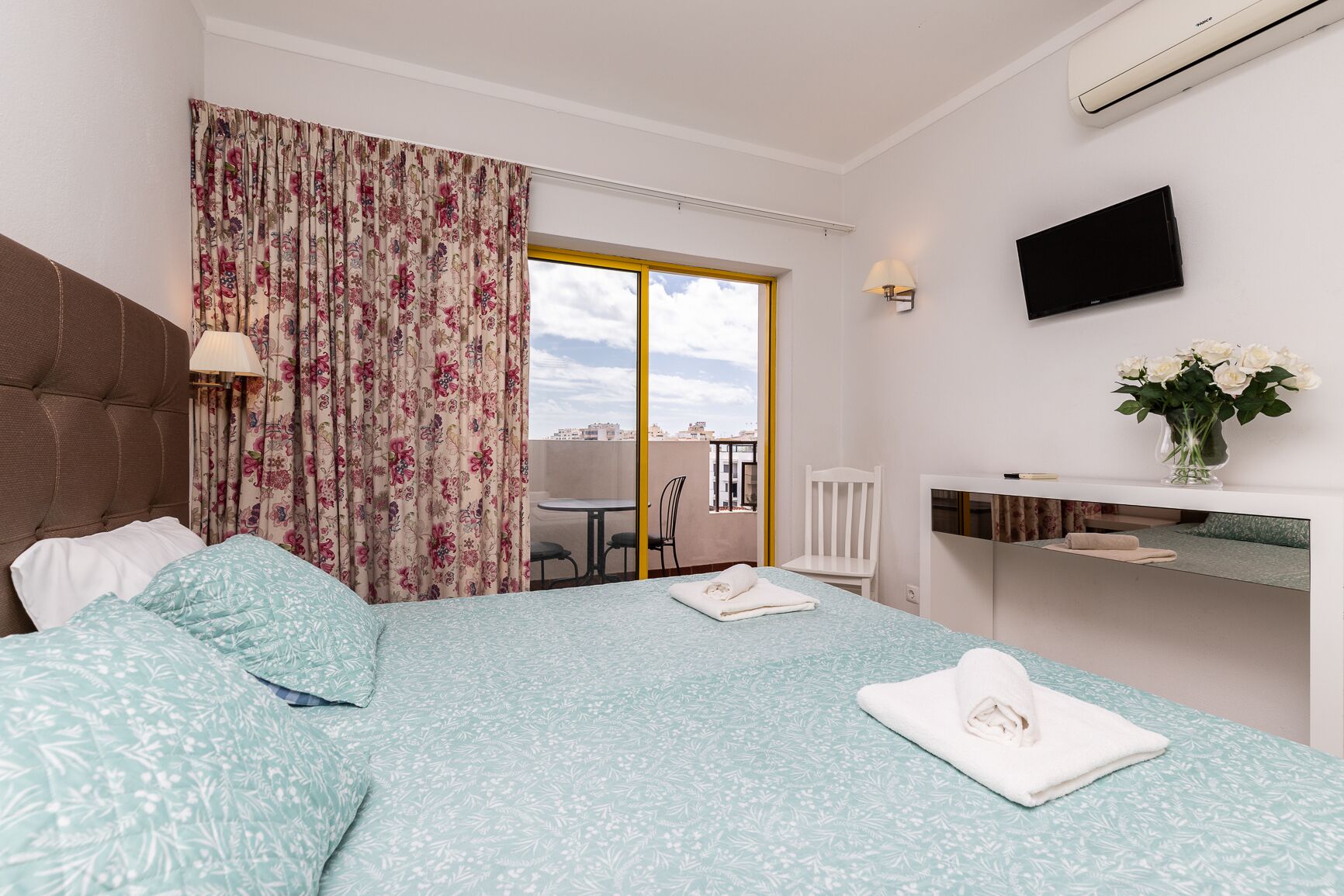 Habitación de hotel con cama, escritorio, silla, televisor y vista a la ciudad.