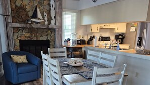 A dining area with a wooden table and chairs, a stone wall with nautical decor, a blue armchair, and a kitchen in the background. - Beautiful Home with direct access to the gulf and private dock!  (Hernando Beach)