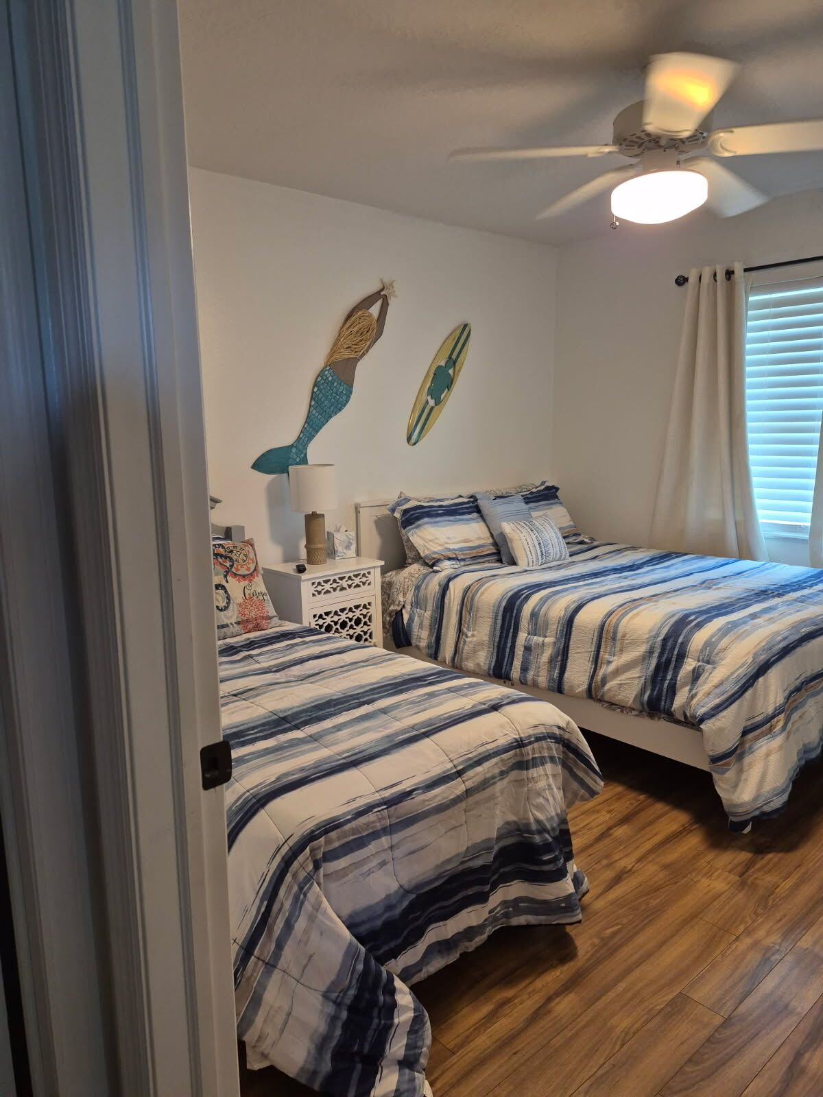 Une chambre avec deux lits, un ventilateur de plafond et une fenêtre avec des stores.