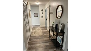 A hallway with wooden flooring, a console table with a sign reading "BEACH HOUSE," and decorative wall art including a star and a striped sign. - Beautiful Home with direct access to the gulf and private dock!  (Hernando Beach)