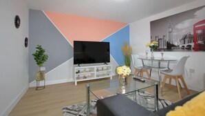 Una sala de estar moderna con un televisor de pantalla plana, una mesa de centro de vidrio y un comedor con una mesa y sillas de vidrio.