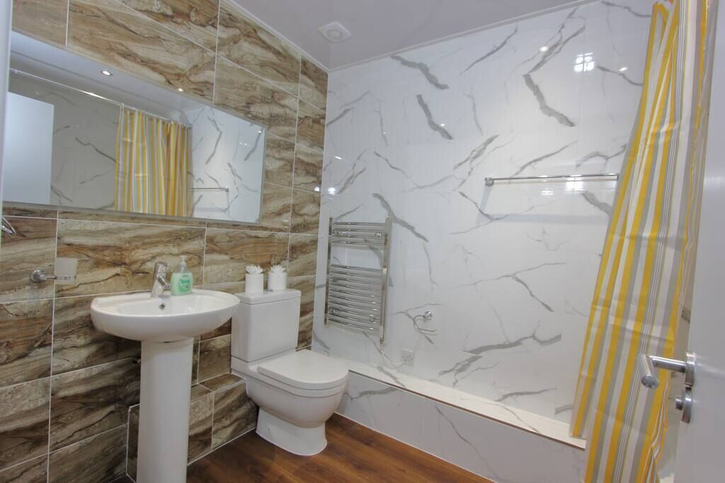 A bathroom with a marble wall, a white sink, a toilet, and a shower with a yellow striped curtain.