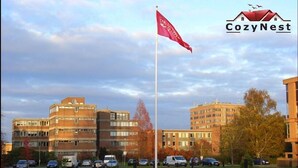 En byggnad med flera våningar, en flaggstång med en flagga och flera parkerade bilar.