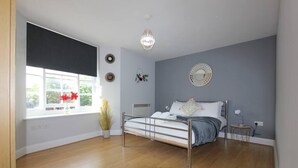 A bedroom with a bed, a window with blinds, a potted plant, and a wall-mounted mirror. - Charming 2 Bed 2 Bath Flat & Parking by CozyNest (Reading)