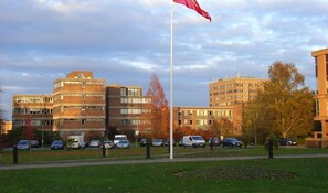 A building with multiple floors, a flagpole with a flag, and several parked cars. - Charming 2 Bed 2 Bath Flat & Parking by CozyNest (Reading)