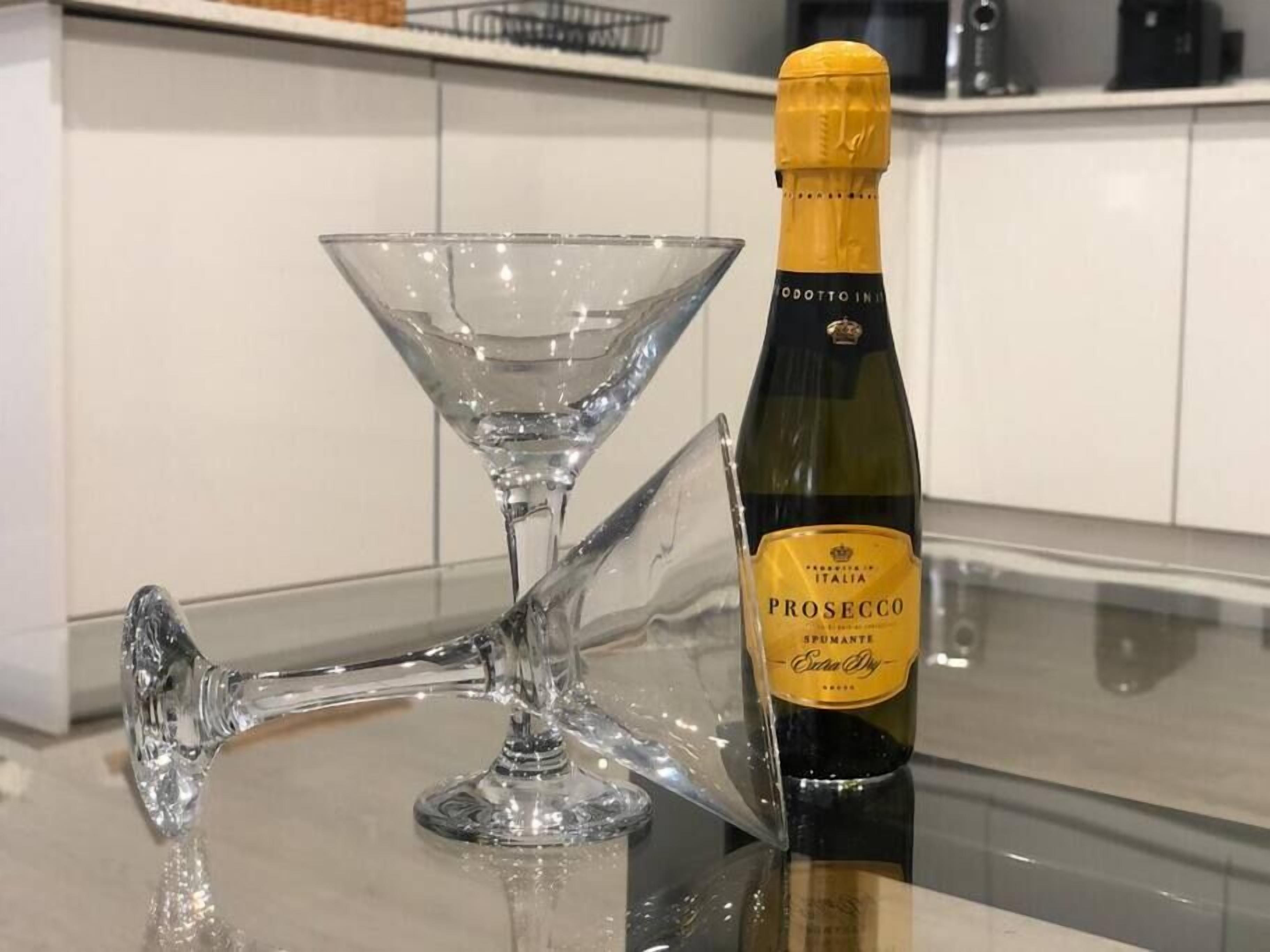Eine Prosecco-Flasche und ein Martini-Glas auf einer spiegelnden Oberfläche.
