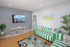 A modern living room with a green and white striped sofa, a flat-screen TV mounted on the wall, and a painting above the sofa.