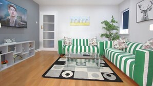 A modern living room with a green and white striped sofa set, a glass coffee table, and a painting of houses on the wall.